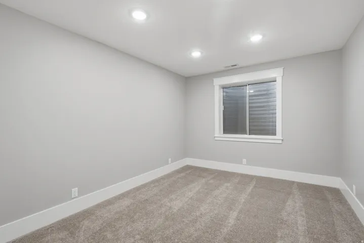Spacious room featuring neutral grey wall paint, plush carpet flooring, recessed ceiling lighting, a white-framed window, and white baseboard trim