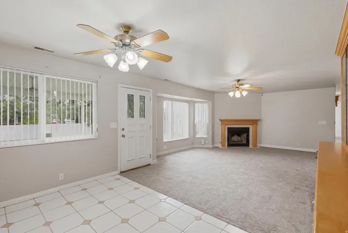 Spacious interior featuring a fireplace with a wood mantel, multiple ceiling fans, and a combination of tiled and carpeted flooring