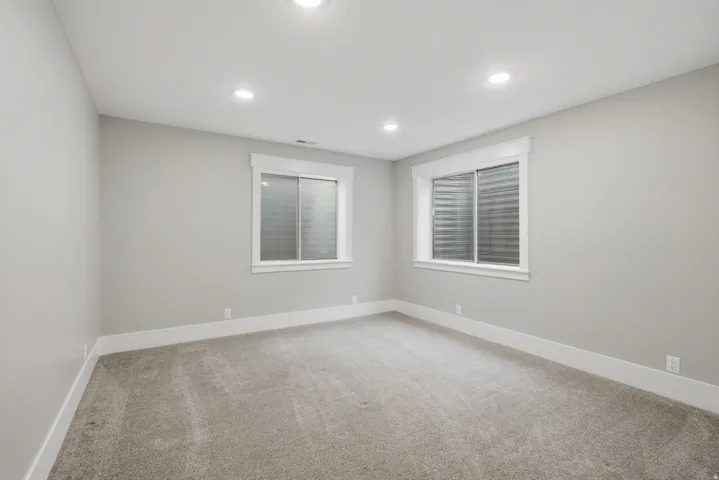 Spacious room with light gray walls, plush gray carpeting, and two egress windows with white trim
