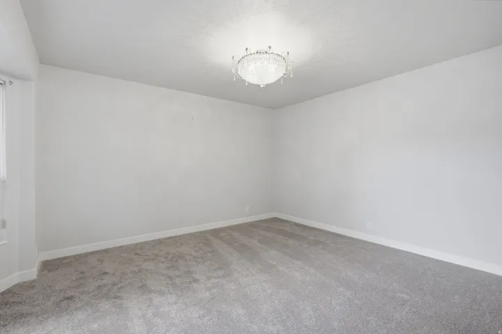 Spacious room featuring a crystal chandelier, neutral wall paint, gray carpeting, and white baseboards