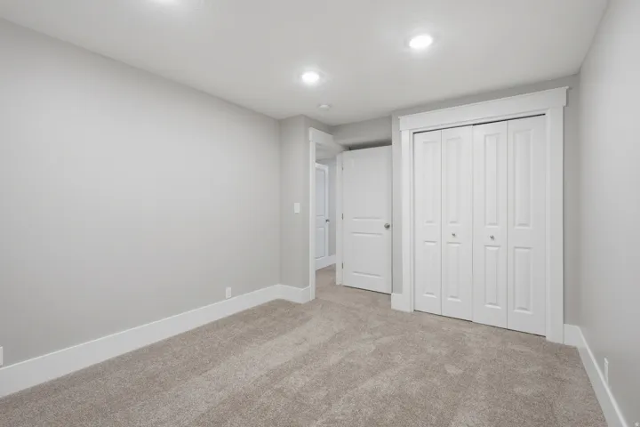 Neutral tone wall color with white trim, recessed lighting, carpet flooring, and bi-fold closet doors