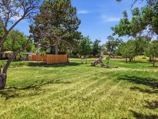 Expansive green lawn with mature trees, established landscaping, and a natural wood fence