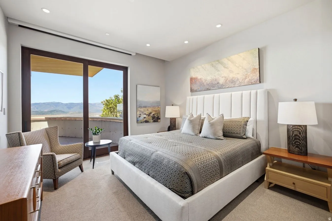 Recessed lighting, light-toned carpeting, full-height sliding glass doors, private balcony access, and a mountain backdrop