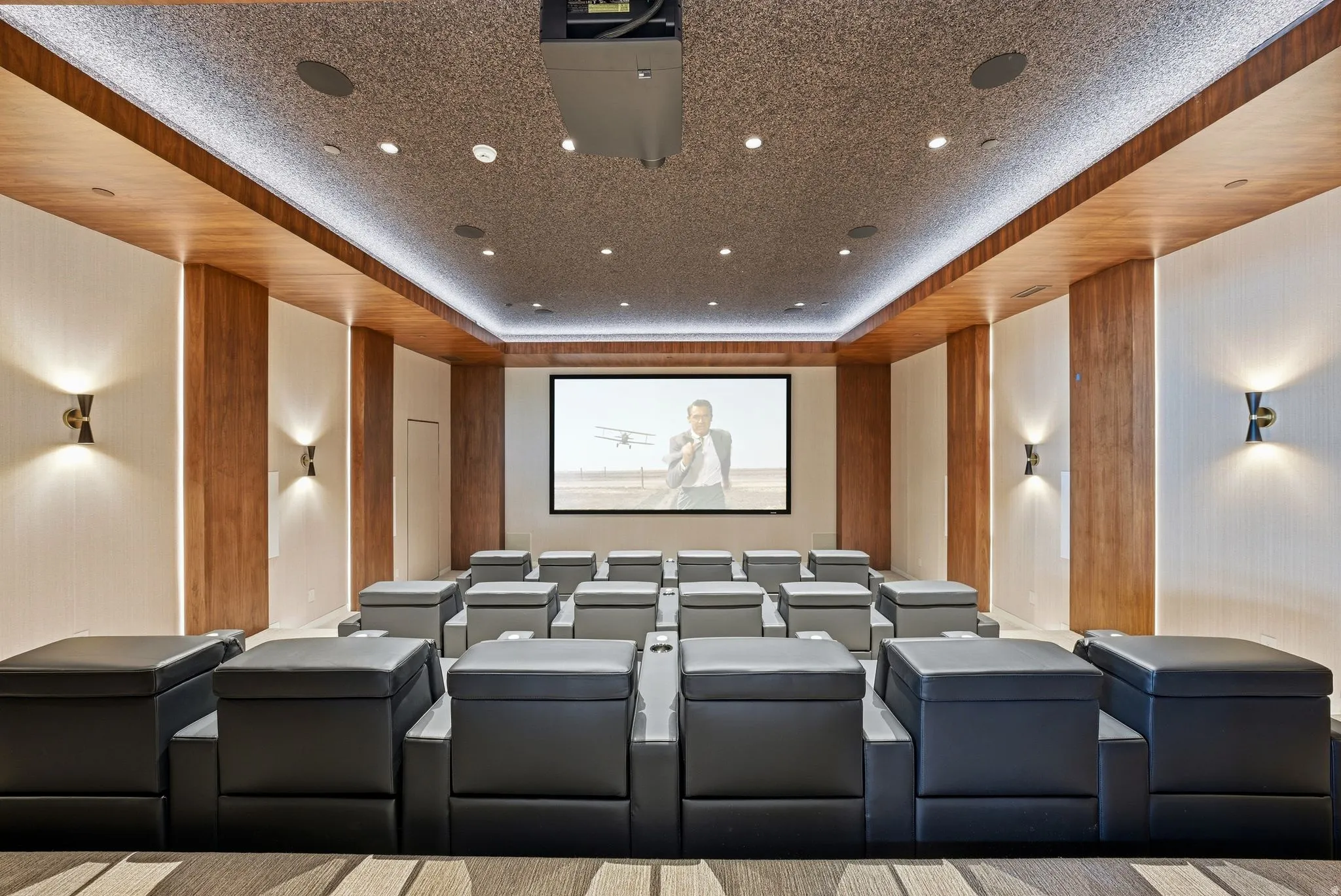 Dedicated media room with a large projection screen, recessed lighting, and wall-mounted sconces