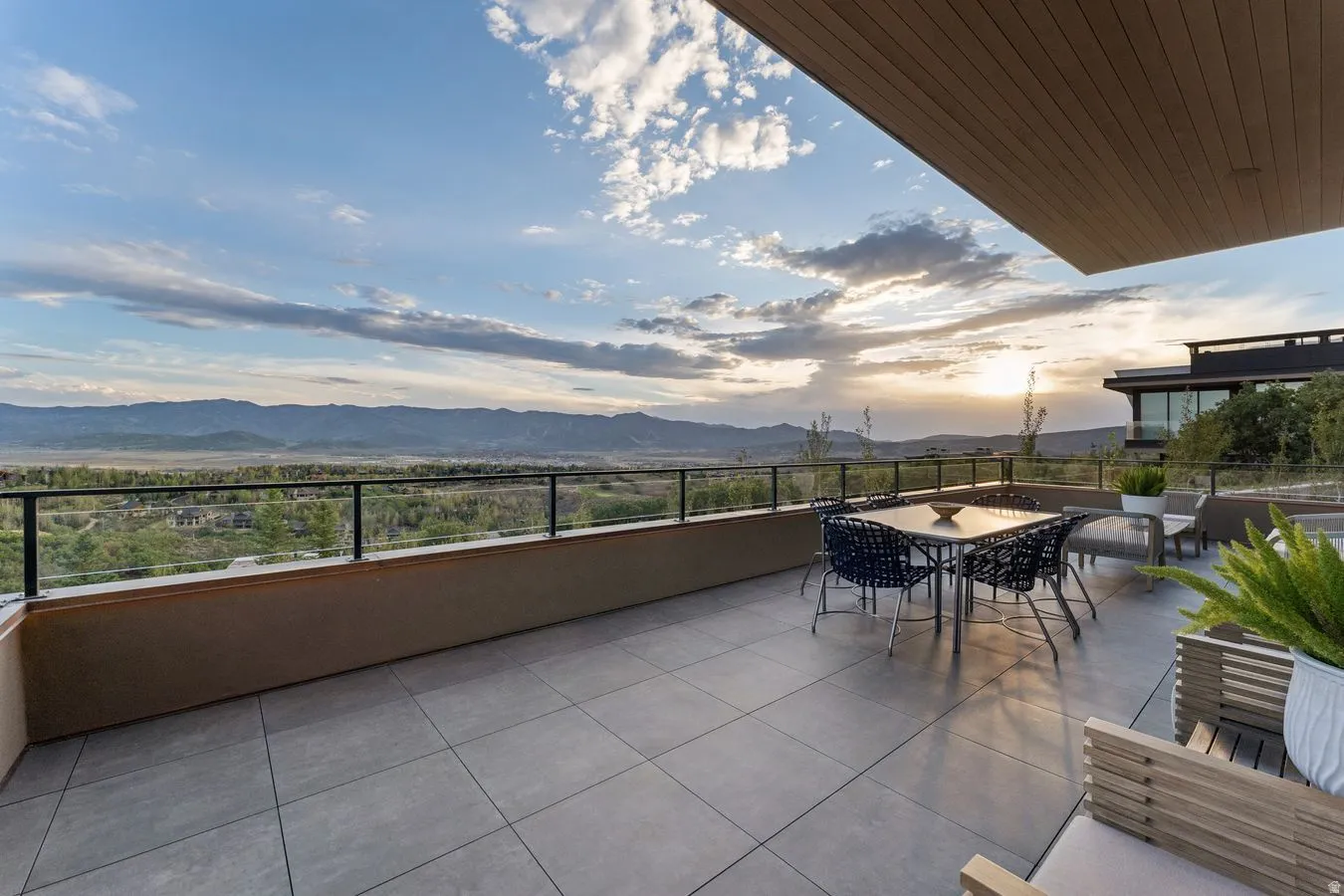 Expansive exterior terrace with large format tile flooring, a glass railing, and a wood-finish soffit