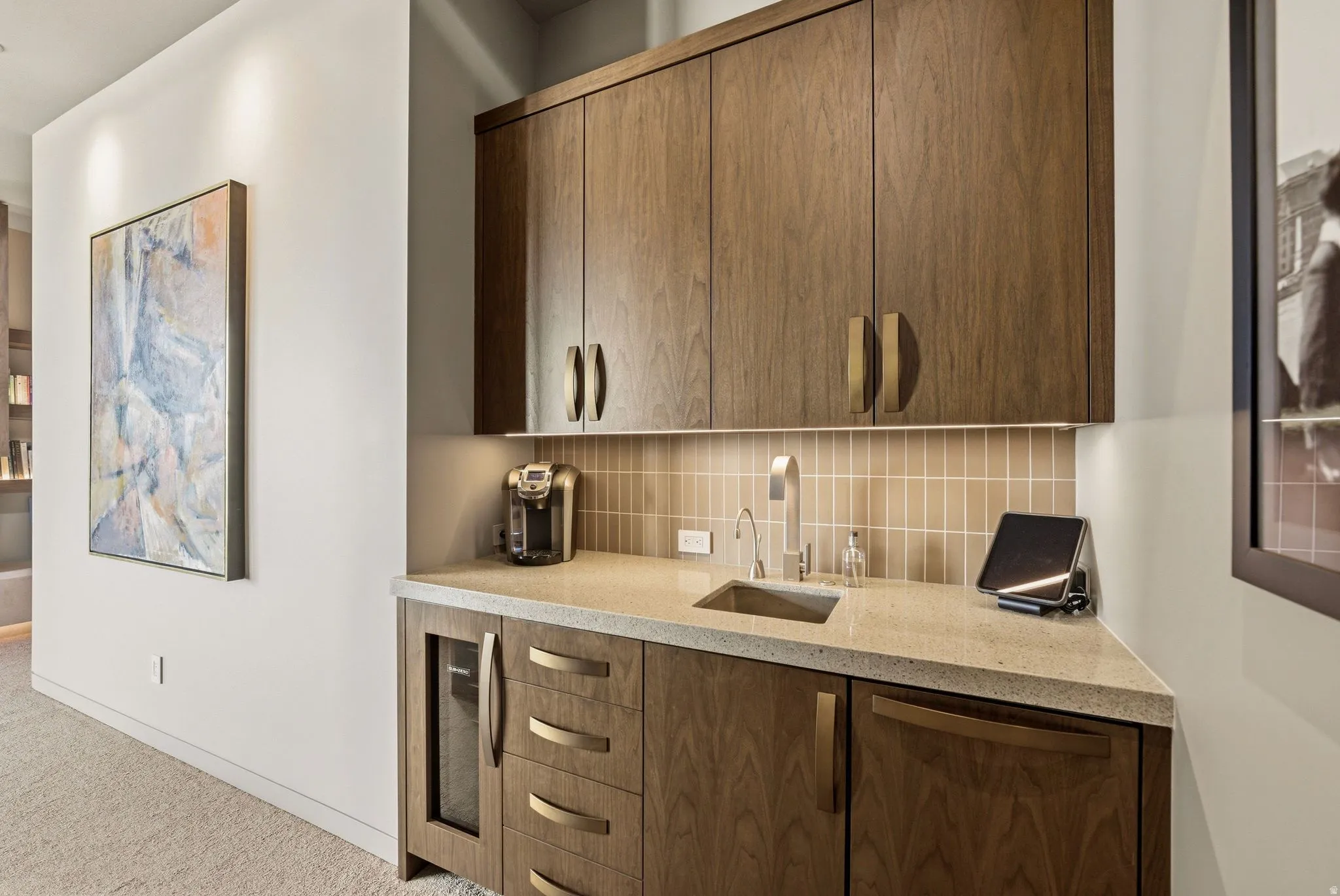 Integrated wet bar featuring wood-finish cabinetry, a stone-finish countertop, under-cabinet lighting, a tiled backsplash, and a stainless steel sink with a gooseneck faucet
