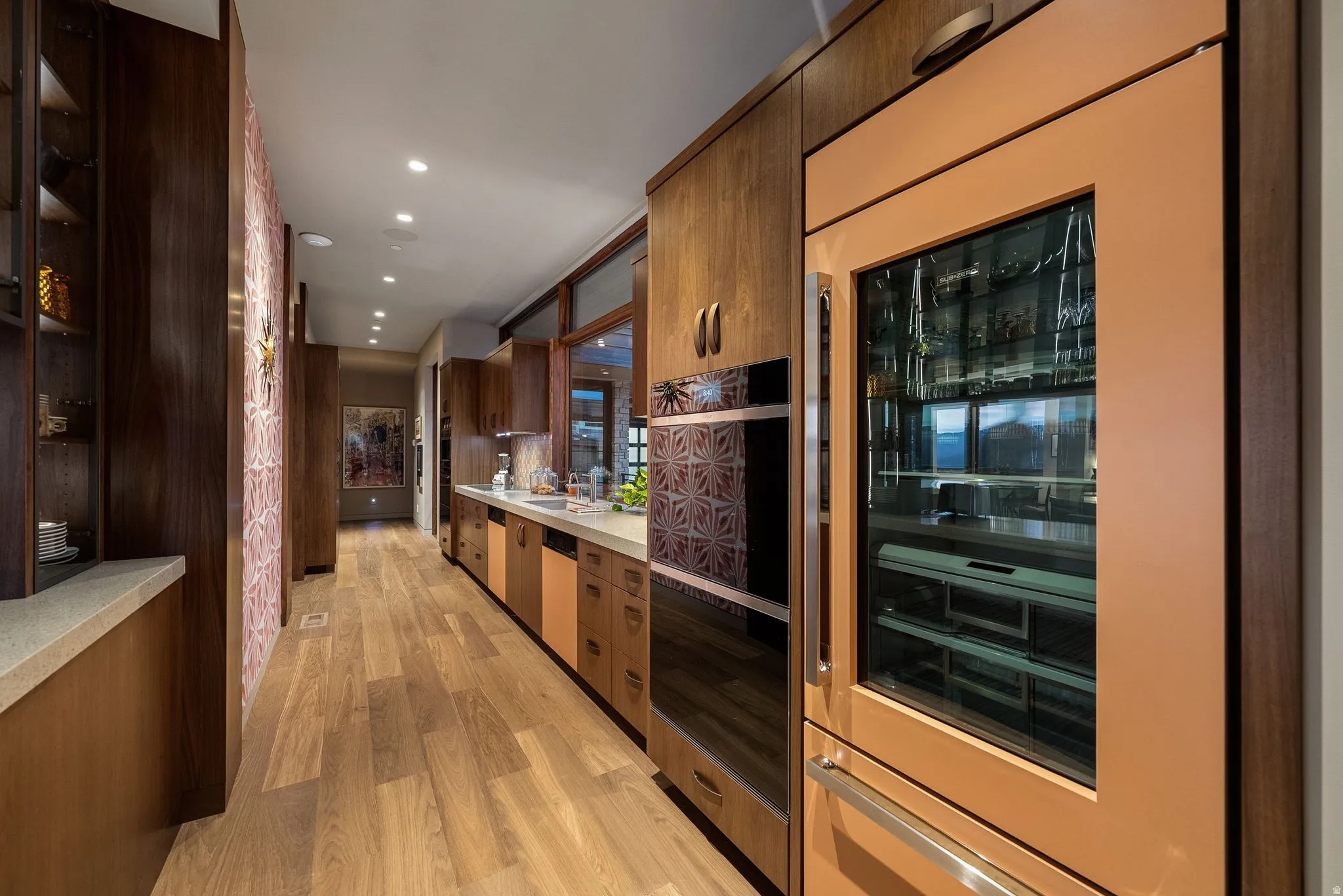 Integrated refrigeration with glass-front display, built-in wall oven, wood-finish flooring, recessed lighting, and custom cabinetry