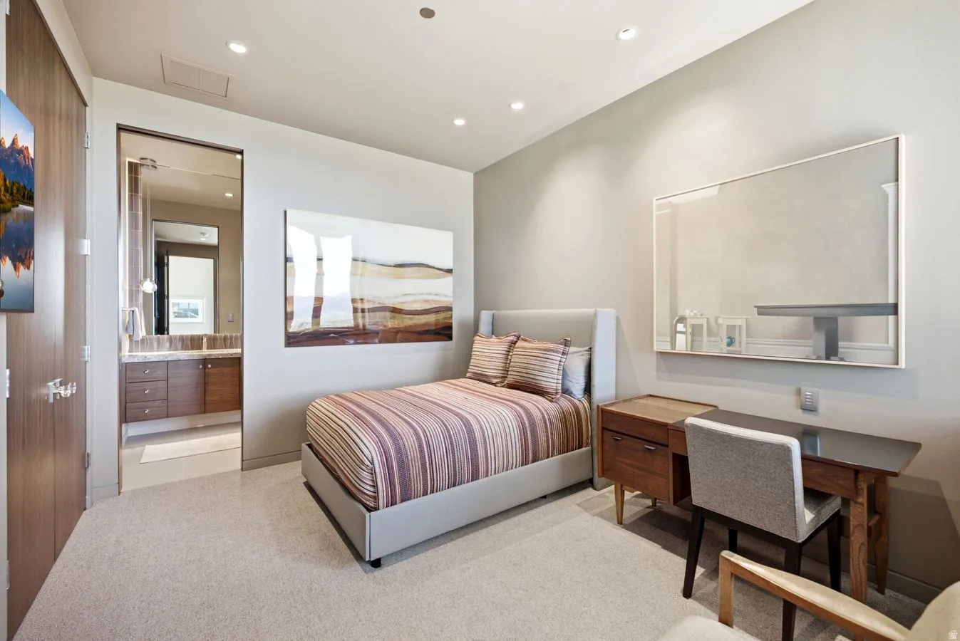 Recessed lighting illuminates the room, featuring plush carpet flooring and a built-in wood-finish desk