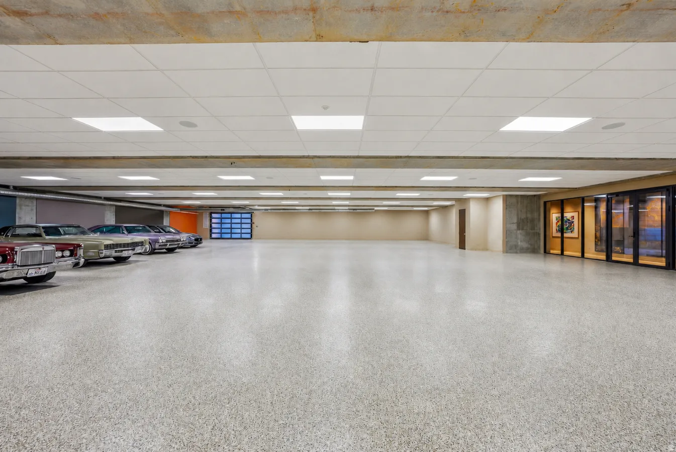 Expansive garage space with a light-colored speckled flooring, overhead square panel lighting, and a glass-paneled garage door
