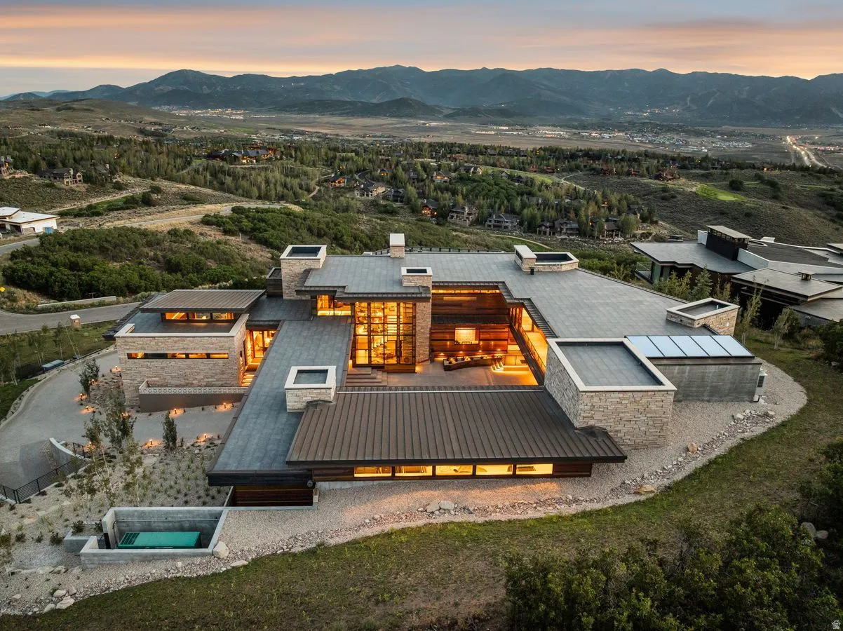 Modern architectural design with stone and metal paneling, extensive window walls, multiple flat roof sections, and a built-in outdoor spa