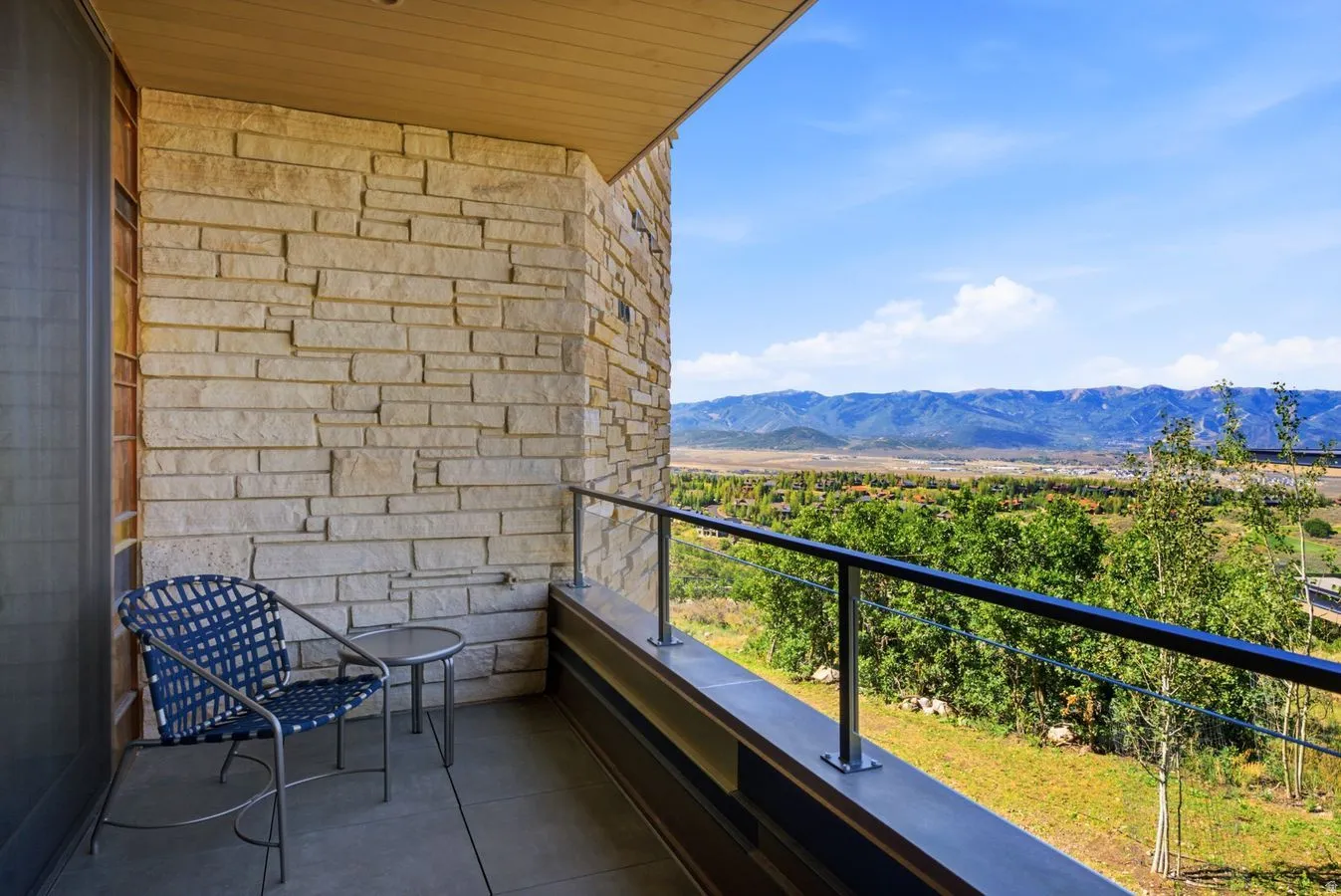 Stone veneer exterior with a concrete balcony featuring a metal and glass railing