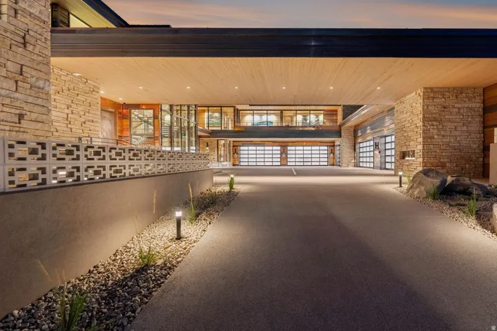 Stone veneer exterior with wood-finish soffit, transparent glass garage doors, and integrated exterior lighting