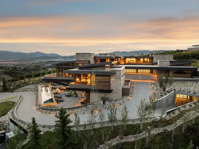 Expansive modern residence featuring stone and wood-finish exterior, large windows, multiple balconies, a long driveway, and an outdoor pool
