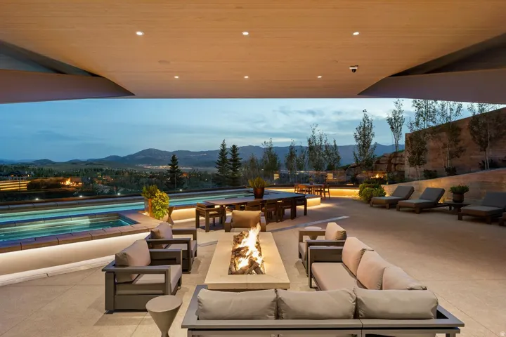 Expansive covered patio featuring a built-in fire pit, multiple seating areas, an outdoor swimming pool, and distinct lighting elements