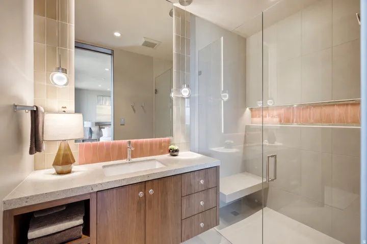 Glass-enclosed shower with integrated bench and niche, wood-finish vanity with countertop, and undermount sink