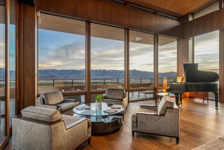 Expansive floor-to-ceiling windows, natural wood-paneled ceiling, wide plank wood-finish flooring, and a large outdoor balcony with metal railings