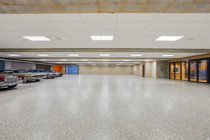 Expansive garage space with a light-colored speckled flooring, overhead square panel lighting, and a glass-paneled garage door