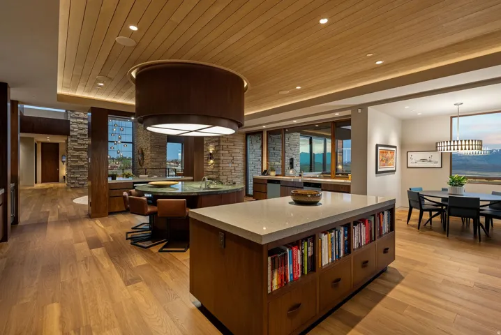 Hardwood flooring throughout, a wood-paneled ceiling with recessed lighting, and a large kitchen island with integrated shelving