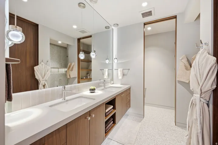Double vanity with integrated sinks, wood-finish cabinetry, full-width mirror, recessed lighting, and speckled flooring