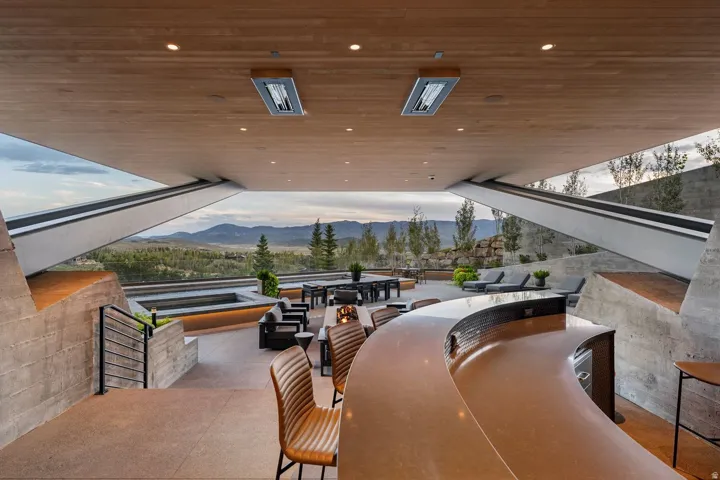 Expansive outdoor living area featuring a built-in curved bar, concrete hardscaping, an in-ground spa, and a wood-paneled ceiling with recessed lighting