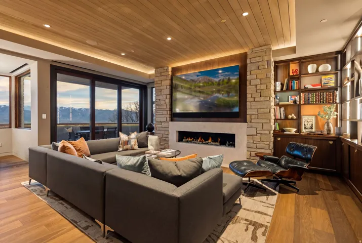 Wood-finish flooring throughout, recessed lighting, stone-clad fireplace with integrated media center, custom built-in shelving, and expansive sliding glass doors