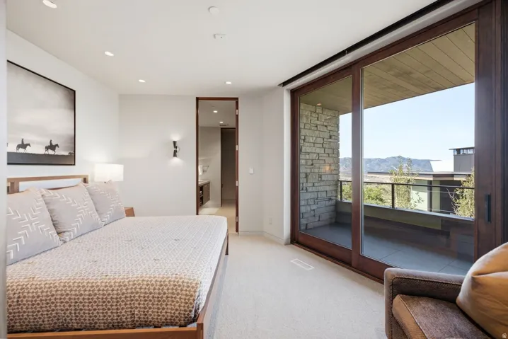Recessed ceiling lighting, wood-framed sliding glass doors, private outdoor balcony, stone accent wall, and wood-finish flooring