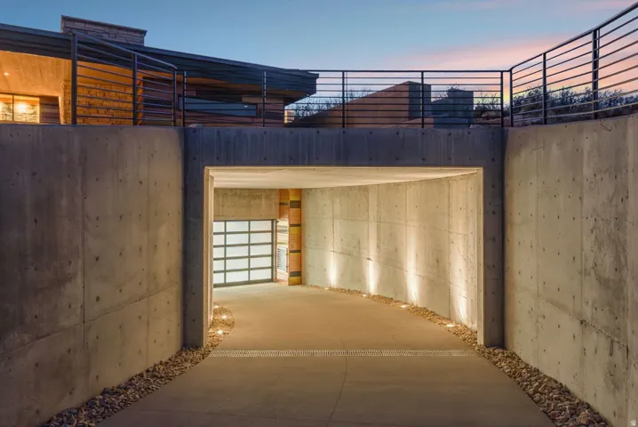Concrete entry tunnel with integrated pathway lighting leading to a glass-panel garage door