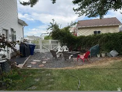 Gravel patio area with a built-in fire pit, surrounded by a mature privacy hedge and a white picket fence
