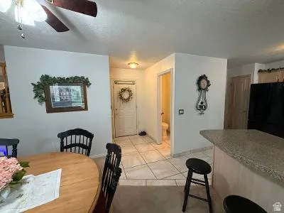Bright kitchen and dining area featuring a ceiling fan with light fixture, a breakfast bar with stone-look countertop, tile flooring, and recessed lighting