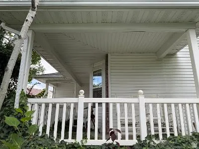Covered porch featuring white siding, white railing, and a window with reflections