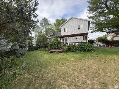 Expansive backyard featuring a manicured lawn and mature trees, with a two-story residence visible in the background