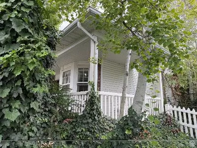 White siding exterior with a bay window, covered porch, and white picket fence