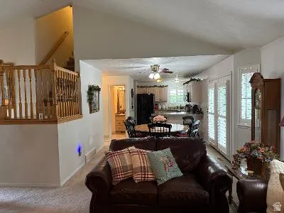 Vaulted ceiling great room featuring a staircase with wood balusters, a kitchen with light wood cabinetry and dark appliances, and a dining area with direct access to an outdoor space via French doors with plantation shutters
