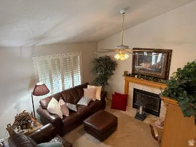 Vaulted ceiling with ceiling fan, fireplace with a tile surround and wooden mantel, and a window with white blinds