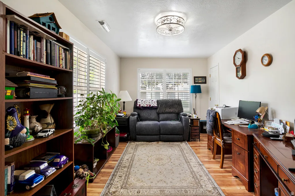 Wood-finish flooring extends throughout this versatile room, featuring multiple windows with louvered shutters