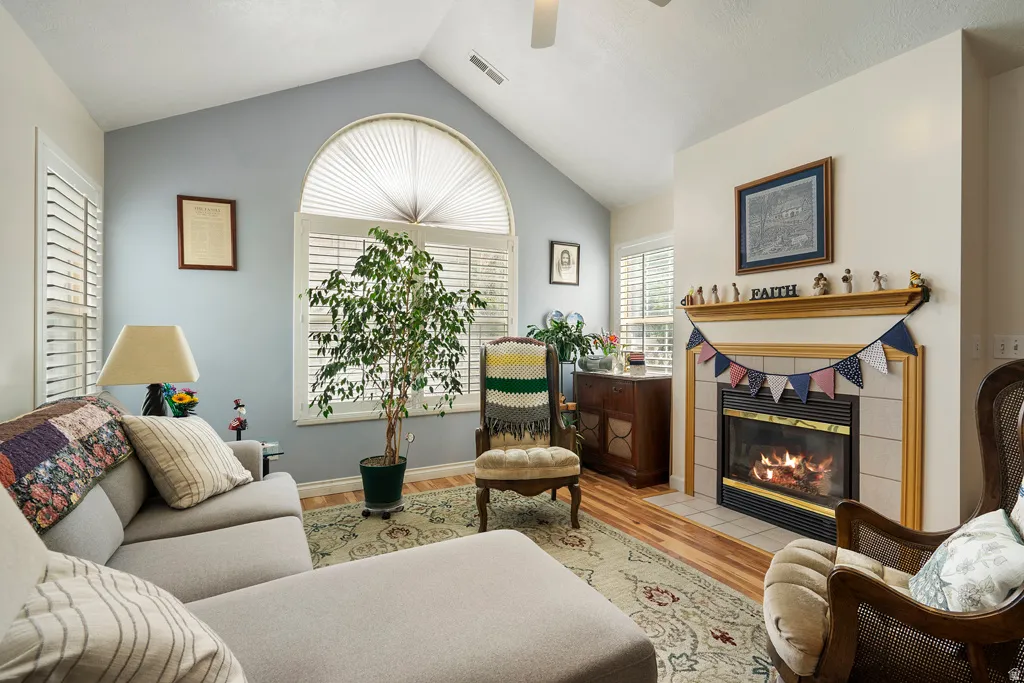 Living room with vaulted ceiling, arched window with plantation shutters, fireplace with tile surround, and wood-finish flooring
