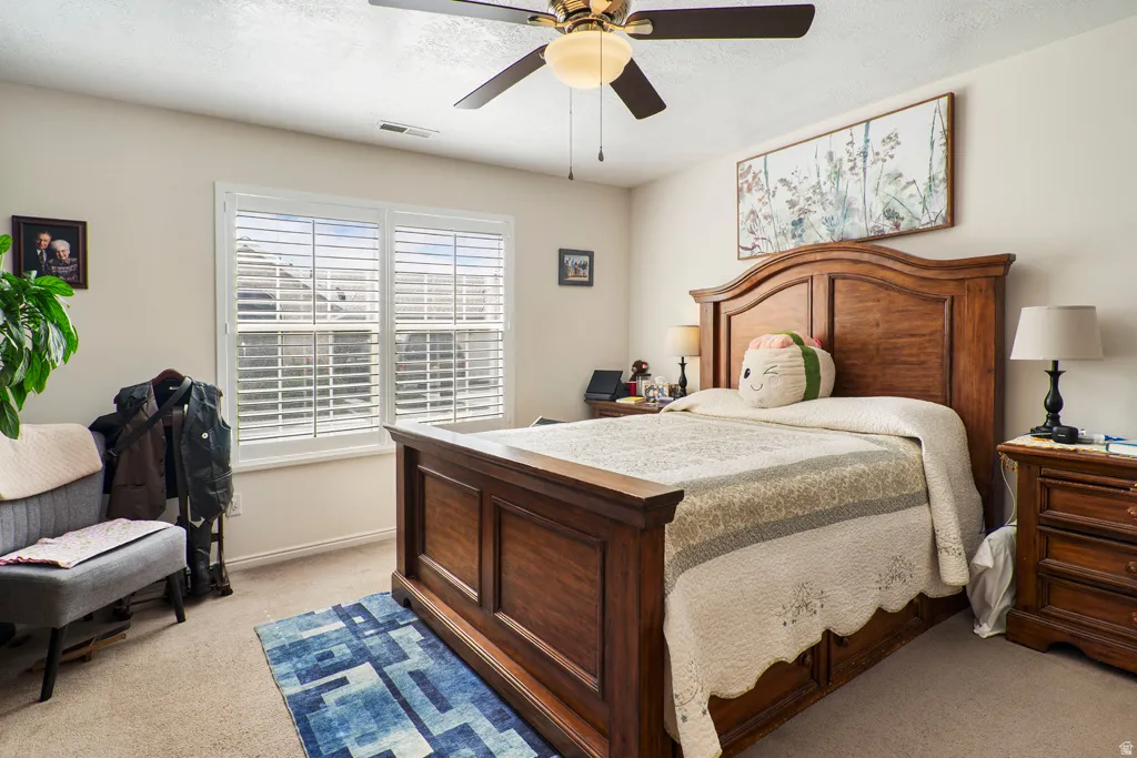 Bedroom featuring a ceiling fan with integrated lighting, a window with white plantation shutters, and light-colored carpet flooring