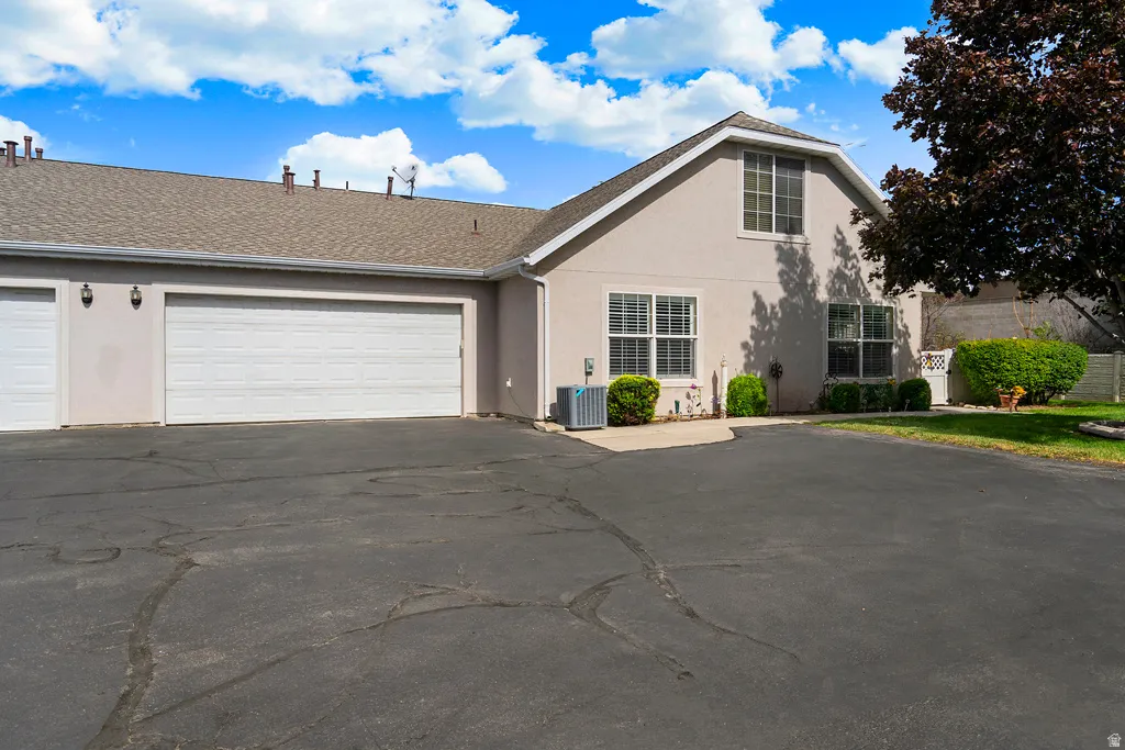 Two-car garage with white paneled doors, stucco exterior, shingle roofing, and a paved driveway