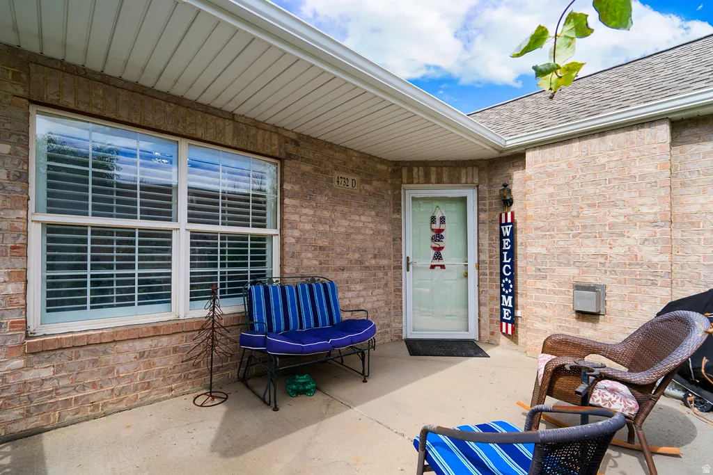 Covered entryway featuring a white storm door, double-pane window with interior blinds, and a brick facade
