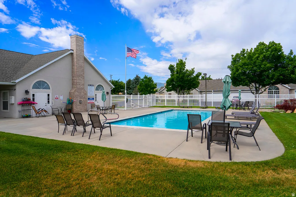 Community swimming pool with surrounding concrete deck, flanked by a clubhouse featuring a stone chimney and arched entryways