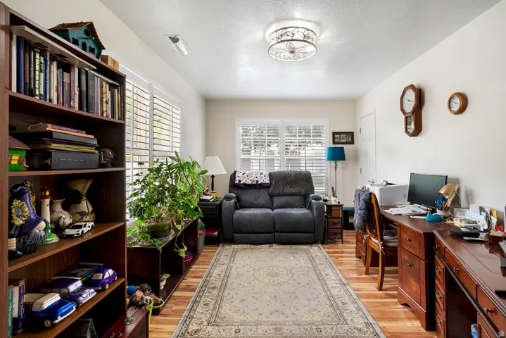 Wood-finish flooring extends throughout this versatile room, featuring multiple windows with louvered shutters