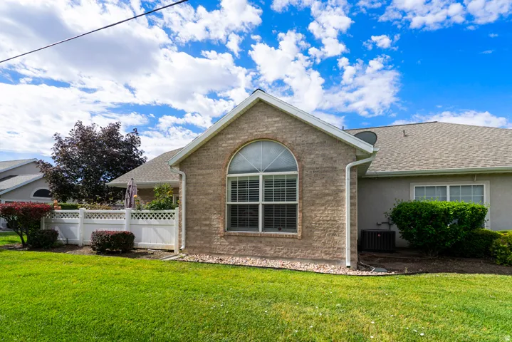 Brick exterior with an arched window, white lattice fencing, a manicured lawn, and mature landscaping