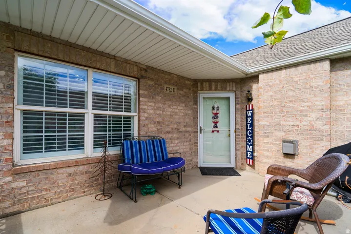 Covered entryway featuring a white storm door, double-pane window with interior blinds, and a brick facade