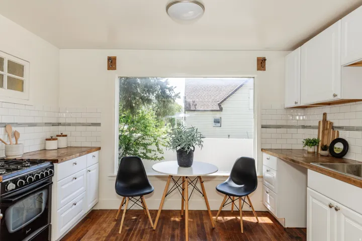 Bright kitchen featuring a large window, white subway tile backsplash with accent band, wood-finish countertops, white cabinetry, and wood-finish flooring