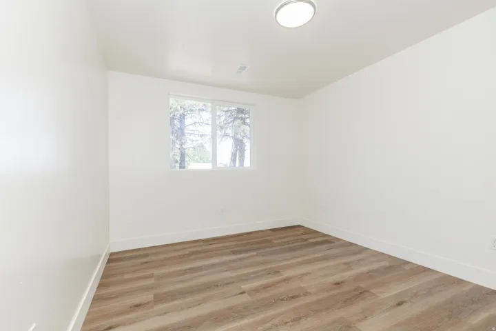 Spacious room with wood-finish flooring, crisp white walls, and a large window providing natural light