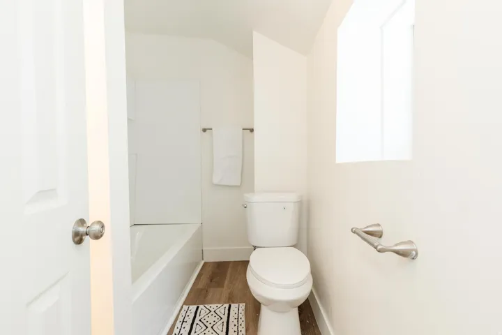 Bathroom featuring a white tub, wood-finish flooring, a white toilet, and a window