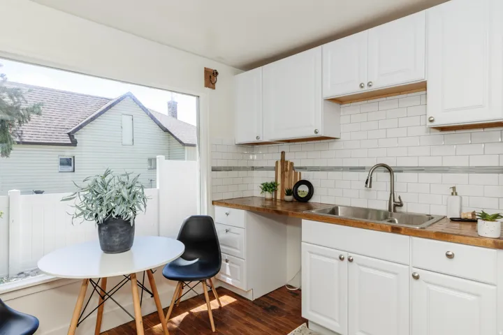 Kitchen featuring white cabinetry, wood-finish countertops, stainless steel double basin sink, and subway tile backsplash with accent band