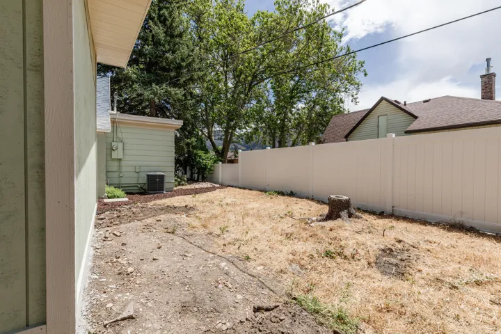 Expansive yard featuring a light-colored privacy fence, mature trees, and a detached structure