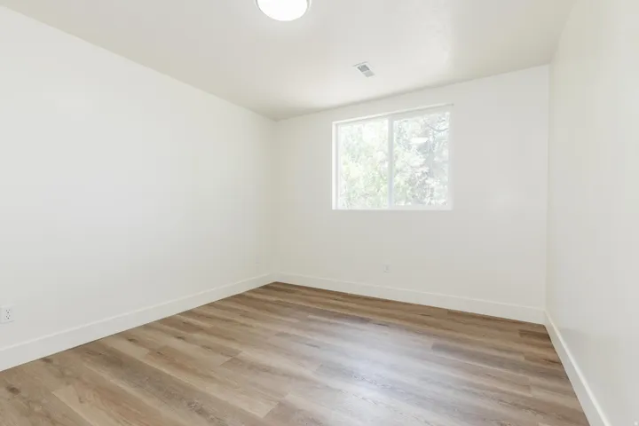 Bright room featuring wood-finish flooring, white walls, clean white trim, and a flush-mount ceiling light