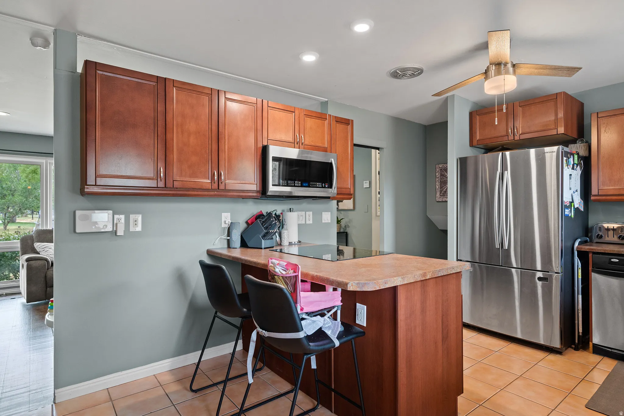Kitchen featuring wood cabinetry, stainless steel appliances, a center island with seating, and ceramic tile flooring